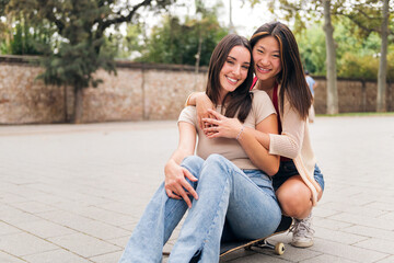 portrait of a young couple of women sitting on a skateboard looking at camera, concept of love and teenager lifestyle, copy space for text