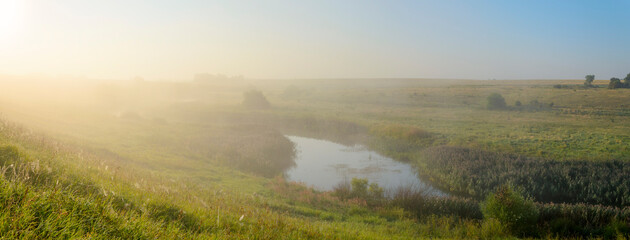Summer foggy morning landscape with green meadows and calm river