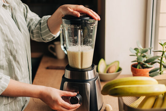 Woman blending spinach, berries, bananas and almond milk to make a healthy green smoothie