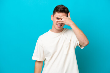 Young handsome Brazilian man isolated on blue background covering eyes by hands and smiling