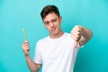 Young Brazilian man brushing teeth isolated on blue background showing thumb down with negative...