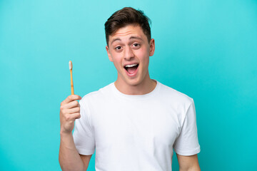 Young Brazilian man brushing teeth isolated on blue background with surprise facial expression