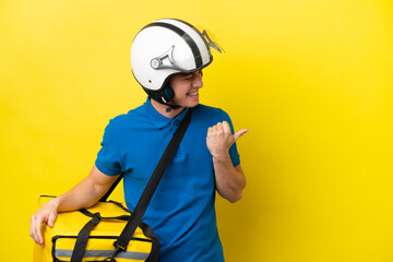 Young Brazilian man with thermal backpack isolated on yellow background pointing to the side to present a product