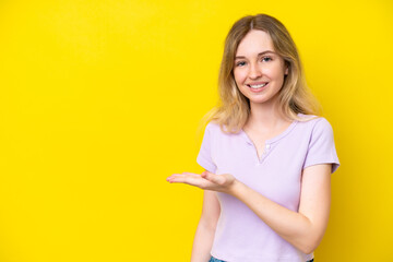 Blonde English young girl isolated on yellow background presenting an idea while looking smiling towards