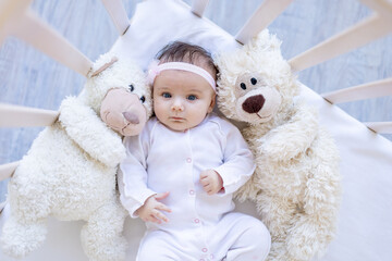 baby girl with teddy bears smiling on the bed on a white cotton bed, falling asleep or waking up in the morning, cute newborn little baby at home in the crib close-up