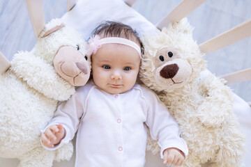 baby girl with teddy bears smiling on the bed on a white cotton bed, falling asleep or waking up in the morning, cute newborn little baby at home in the crib close-up
