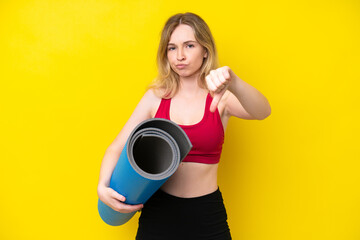 Young sport caucasian woman going to yoga classes while holding a mat isolated on yellow background showing thumb down with negative expression