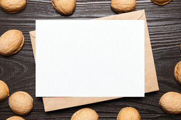 Blank card mockup with walnut shells and envelop on wooden background, top view, flat lay. White holiday card on brown table