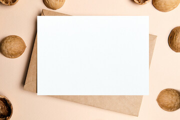 Blank card mockup with walnut shells and envelop on beige background, top view, flat lay. White holiday card mock up with shell decoration