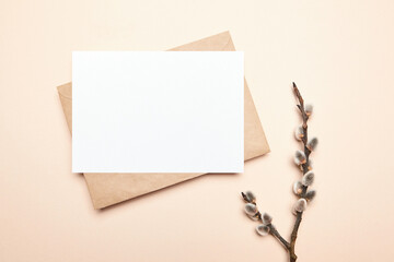 Greeting card mockup with branch of pussy willow and envelop on beige background, top view, flat lay. Blank Easter Holiday card with catkins