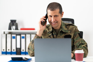 Handsome American soldier behind his computer talking on the phone at office
