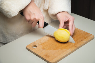 Step by step potato recipe. Hands holding and cutting raw potatoes on a wooden cutting board. Housewife wife is ready to eat food at home in the kitchen