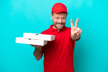 Pizza delivery man with work uniform picking up pizza boxes isolated on blue background smiling and showing victory sign