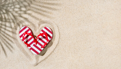 Pare of red flip-flops in shape of heart on sand with palm leaves shadow, copy space, tropical...