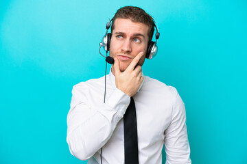 Telemarketer caucasian man working with a headset isolated on blue background having doubts and with confuse face expression