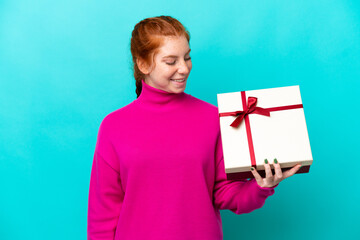 Young caucasian reddish woman holding a gift isolated on blue background with happy expression
