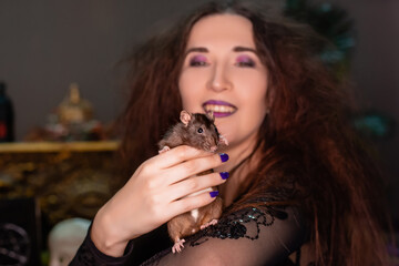 Close-up of a black rat in the hands of a witch in black clothes with disheveled hair. Halloween witch.