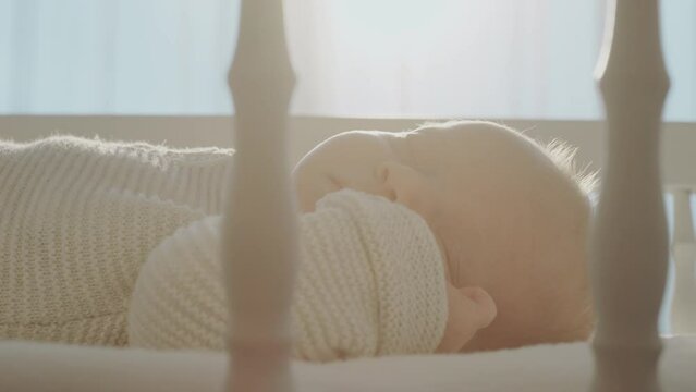 Close up of a caucasian baby boy sleeping in his crib against a large window and sunlight coming through the window