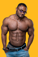 Strong African guy with big biceps and great abs standing with his hands in jeans pockets. Awesome muscular torso of a dark-skinned man. 