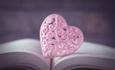 Pink heart on an open book. Valentine's day concept with blurred dark background. Toning.