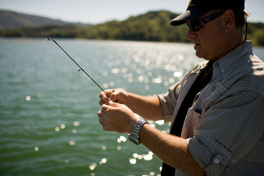 A Man Stands On A Boat With Fishing Pole In Hand While Bass Fishing In Lake Casitas.