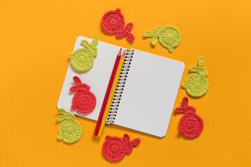 White empty notebook with crochet Easter bunnies on a yellow backgound. Top view. Copy space.