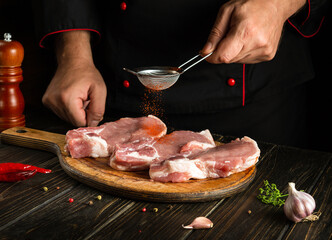 Professional chef adds paprika to raw meat ribs before grilling. Work environment on the kitchen table with spices and condiments