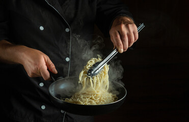 Professional chef fries spaghetti in a hot pan. Space for advertising on a black background. Italian national cuisine