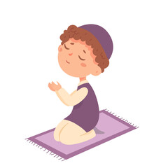 Cute boy praying, child in traditional hat sitting on knees on floor rug to pray to God