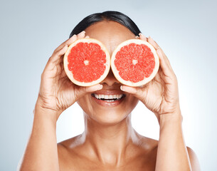 Funny, fruit and woman use grapefruit for a joke covering her eyes isolated against a studio blue background. Health, beauty and skincare model smiling due to vitamin c from juicy citrus