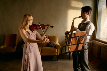 Young female violinist and male saxophonist training at home