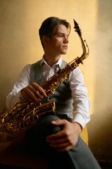 Naklejka premium Young man sitting on chair with saxophone