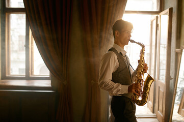 Young elegant man playing gold alto saxophone in misty room