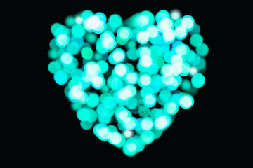 Blurred Cyan colour confetti of lights in the shape of a heart on a black background (backdrop for valentine's holiday)
