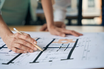 Hard-working woman holding pencil and looking at huge paper
