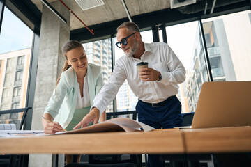 Joyous woman and her office collegue discussing paperwork on table