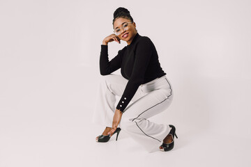 Cheerful African American woman squatting on white background and smiling with hand on her face