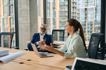Enthusiastic lady in business suit explaining work project to coworker