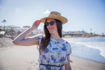 A girl on vacation at the beach smiling with sunglasses and a summer hat.