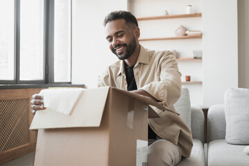 Happy young man opening parcel at home, handsome guy open package indoor, delivery, shipment,...