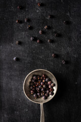 Big old spoon with juniper berries on black background