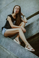 Naklejka premium teenage girl with long hair poses; slender figure of a beautiful girl with emotional facial expressions; sunglasses on the head; a person against the background of a city landscape;