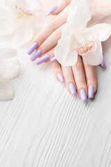 Obraz na płótnie Canvas Girl's hands with delicate purple manicure and orchid flowers