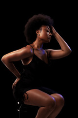 Fototapeta na wymiar Studio portrait of elegant african american lady with curly hair afro hairstyle against black background. Girl in black dress.