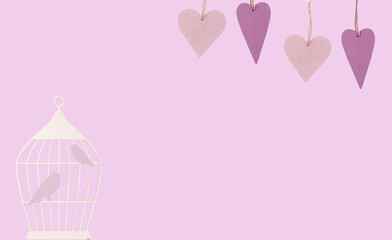 Lilac wooden figurines of hearts and Silhouette of a cage with birds  on a lilac background. Banner. Lots of empty space.. Easter, spring, valentine's day concept. two birds in a cage and hearts.
