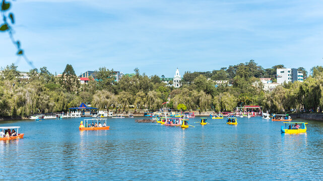 Baguio City, Philippines - Tourist enjoy rowing small boats at a man-made lake in Burnham Park. The cityhall and skyline visible in the back.