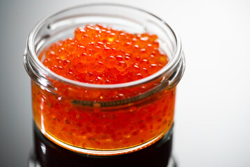 Red caviar in a glass jar, close up. Salmon caviar on black background. Delicious gourmet food.  Delicatessen. Texture of caviar. Seafood, macro shot. 