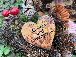 Grabschmuck auf dem Friedhof im Herbst und Winter mit einem Herz und der Inschrift:  Geliebt und...
