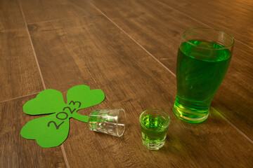 shot and pint glasses on wooden bar background filled with green spirit cocktail and shamrock,...