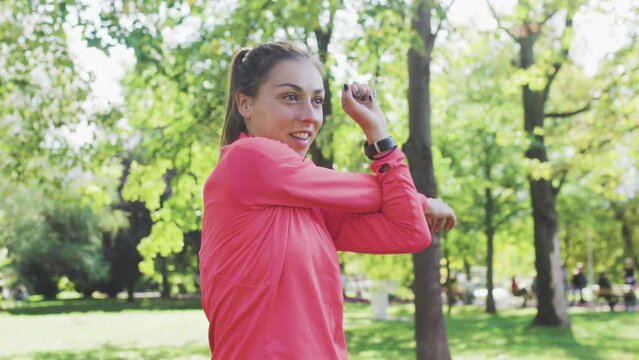 Fitness girl stretching her arms and neck in the park. Warming up exercise before running